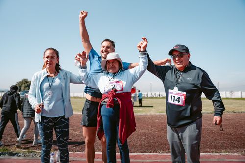 Free Four adults joyfully celebrating after completing a race, holding medals outdoors. Stock Photo
