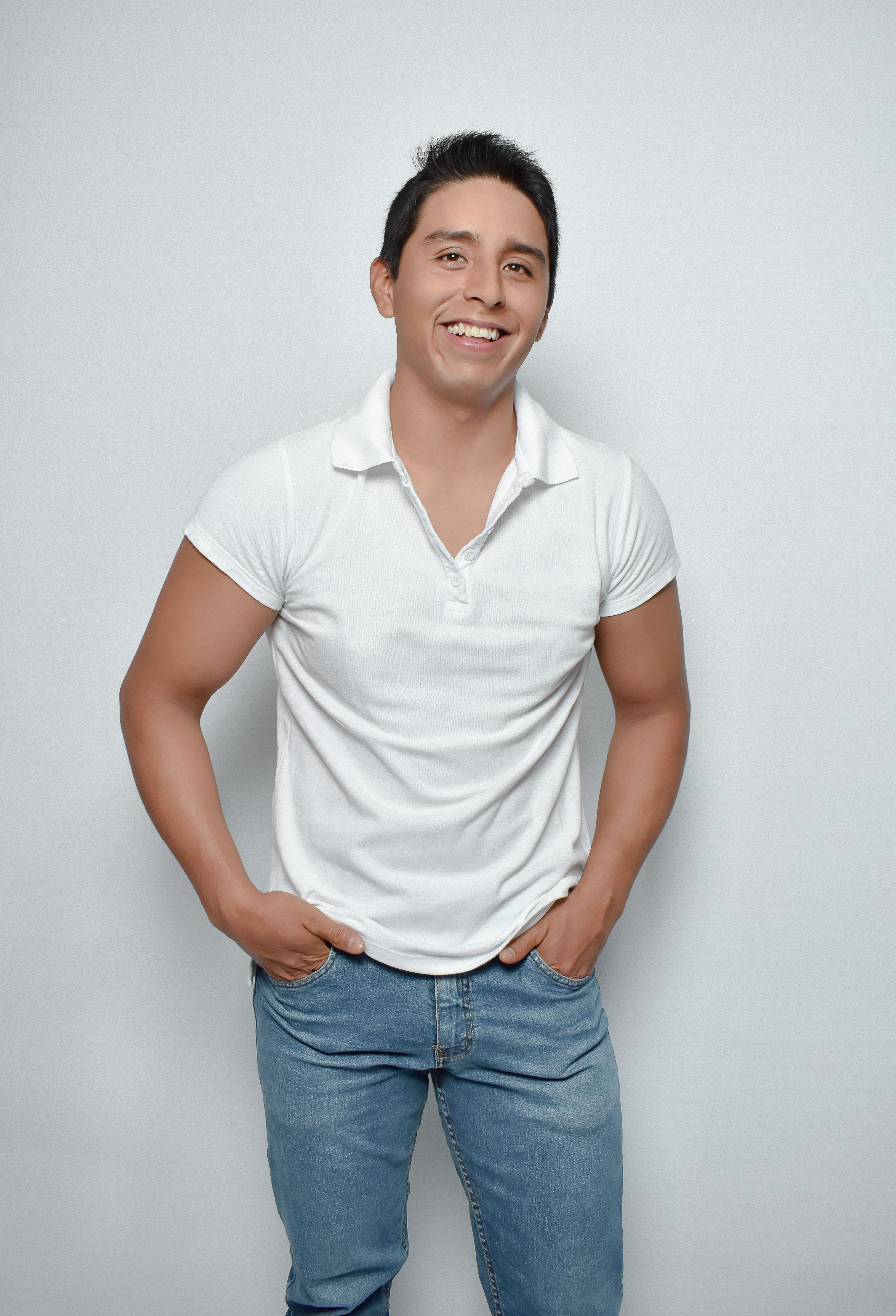 Smiling young man posing in a white Polo T-shirt and jeans in a studio.