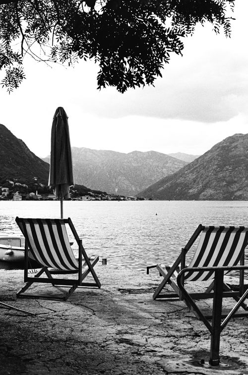 Free Serene black and white image of a lakeside retreat with sunloungers and mountains in the background. Stock Photo