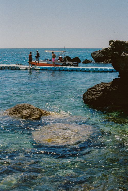 Free People enjoying leisure on a jetty with a boat by a rocky coastline during summer. Stock Photo