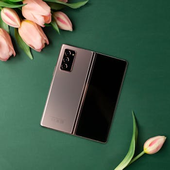 Foldable smartphone on green background with pink tulips, showcasing modern technology and elegance.
