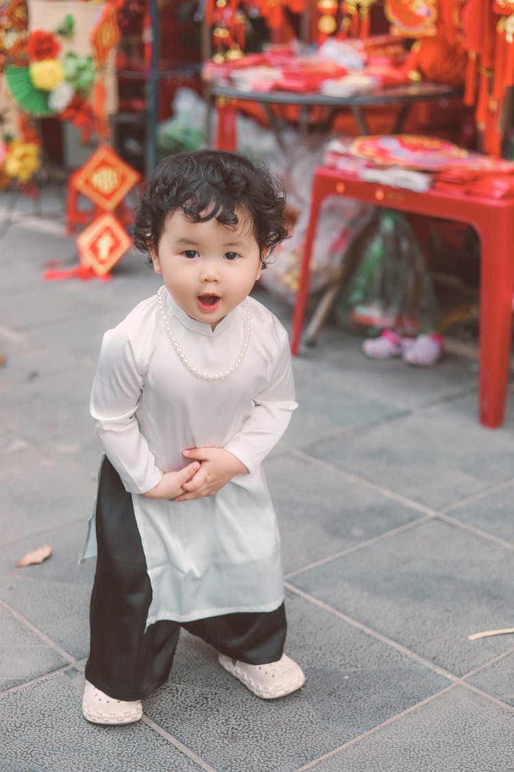 Happy Child In White Tunic Standing On Sidewalk