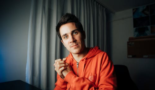Man in Hoodie Sitting with Hands Clasped