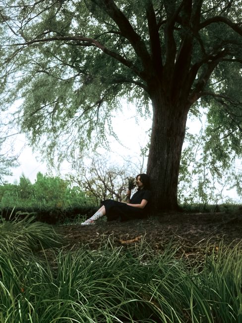 Adult woman sitting under a large tree in a meadow, enjoying a peaceful moment outdoors.