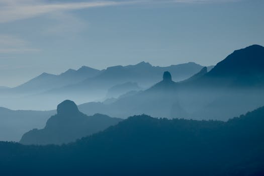 A serene landscape of misty mountains under dawn light, featuring rolling hills and fog.