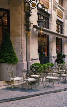 A picturesque outdoor café with elegant metal chairs and ornate architecture on a cobblestone street.