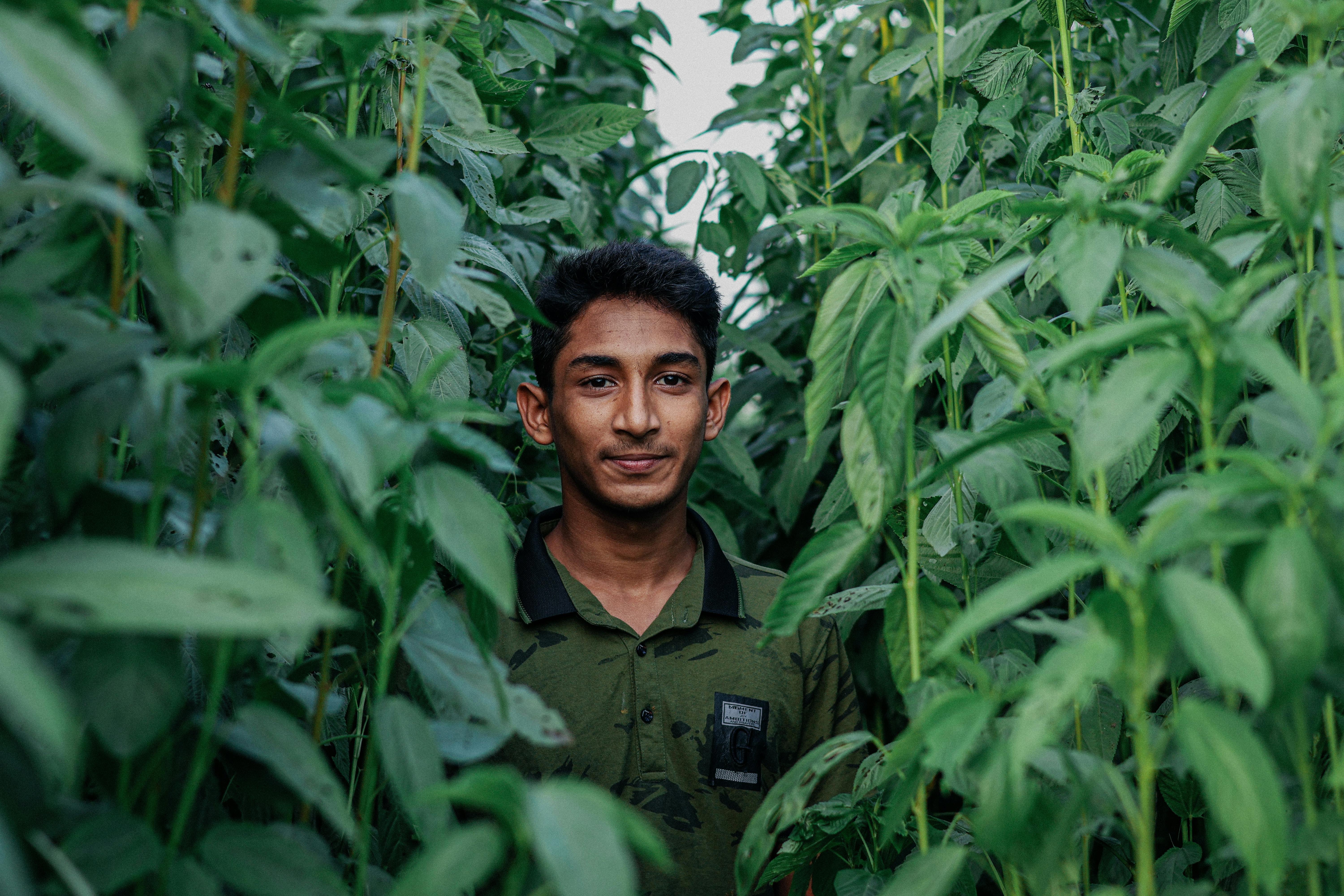 Portrait of a young farmer smiling amidst green crops in Pabna, Bangladesh, showcasing local agriculture.