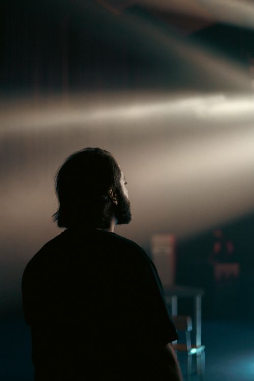 Free A man with black hair and beard stands under concert lights, creating a dramatic mood. Stock Photo