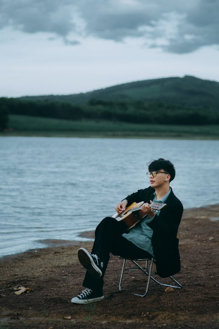 Man Sitting On A Chair On A Beach Playing His Guitar