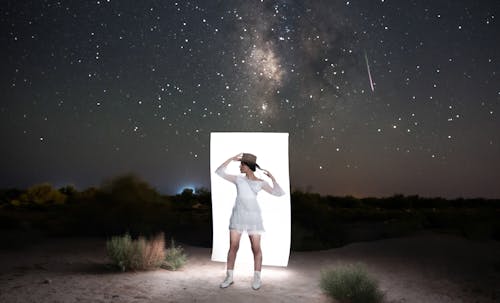 Model in a White Mini Dress and Cowboy Hat in Front of a Rectangle of Light Against the Starry Night Sky