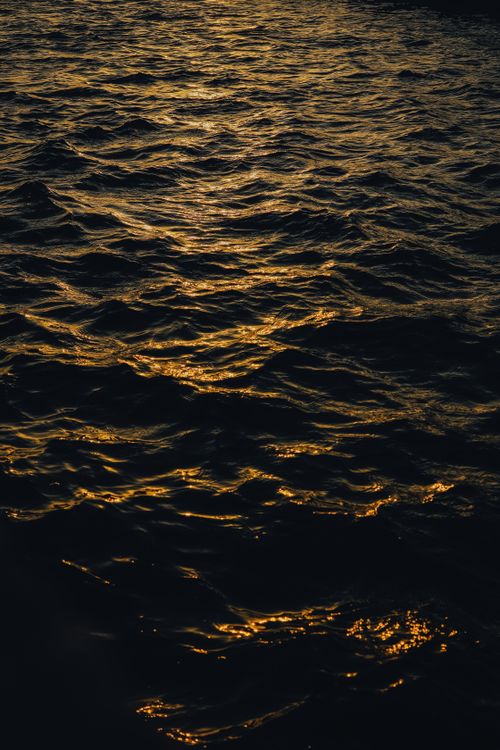 Free A stunning view of golden sunlight reflecting on rippling water at sunset, creating a mesmerizing texture. Stock Photo