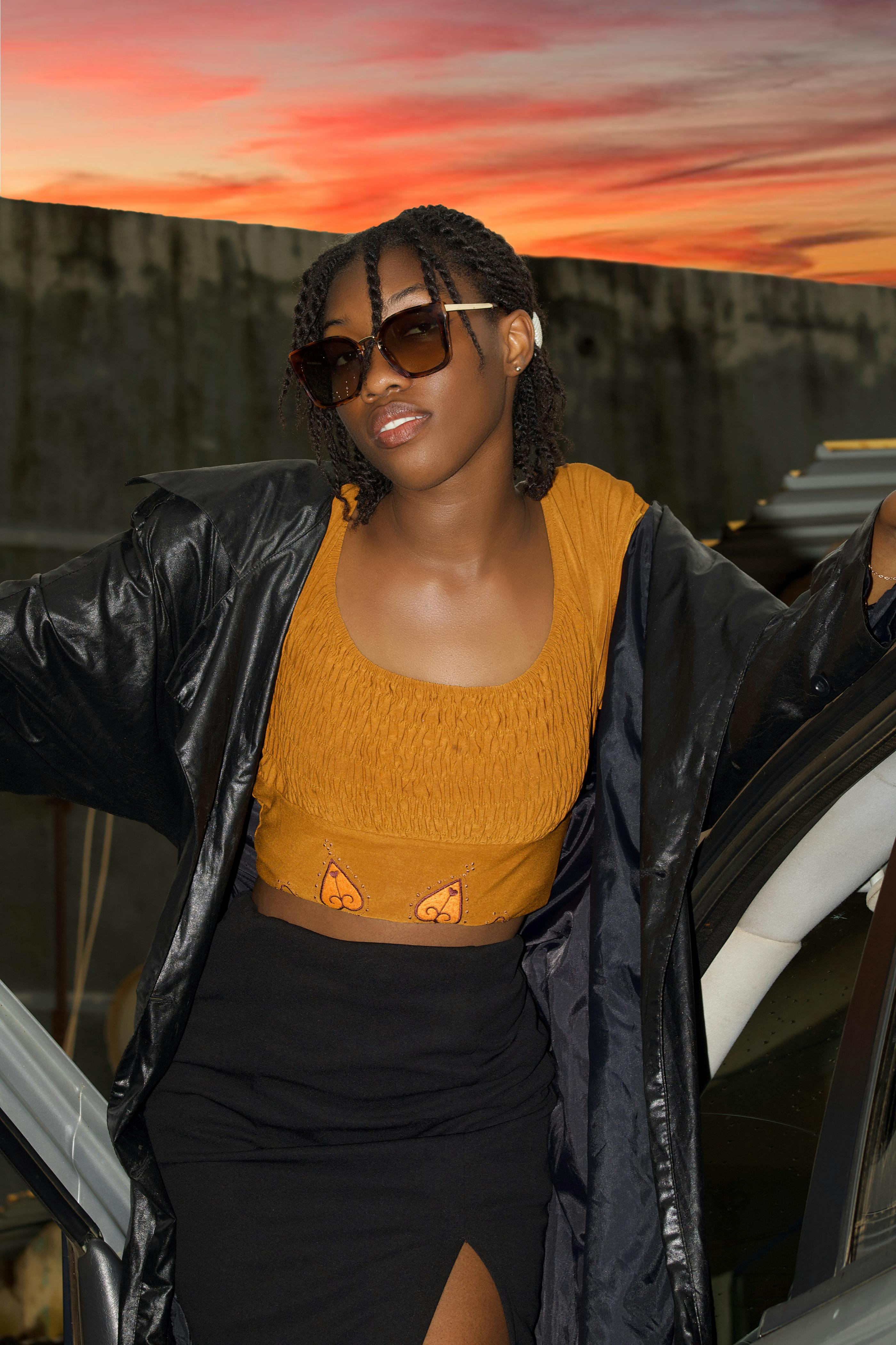 De franc Model Amb Un Crop Top Groc I Un Abric Negre Posant Al Capvespre Foto d'estoc