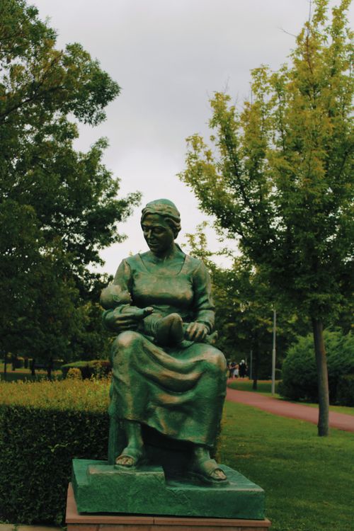 Free A tranquil statue of a woman with a baby in an urban park setting. Stock Photo