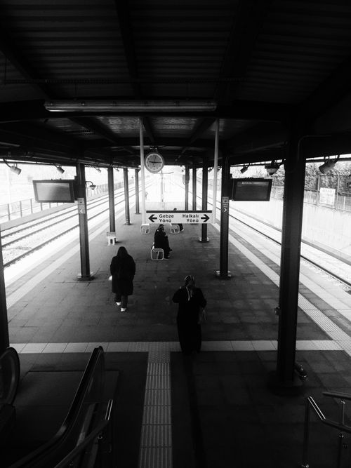 Free A dramatic black and white photograph of an urban railway station with travelers waiting on the platform. Stock Photo