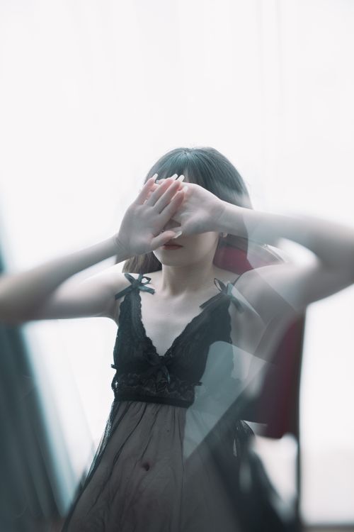 Free Portrait of a woman wearing sheer black nightwear, covering face with hands, creating a mysterious mood. Stock Photo