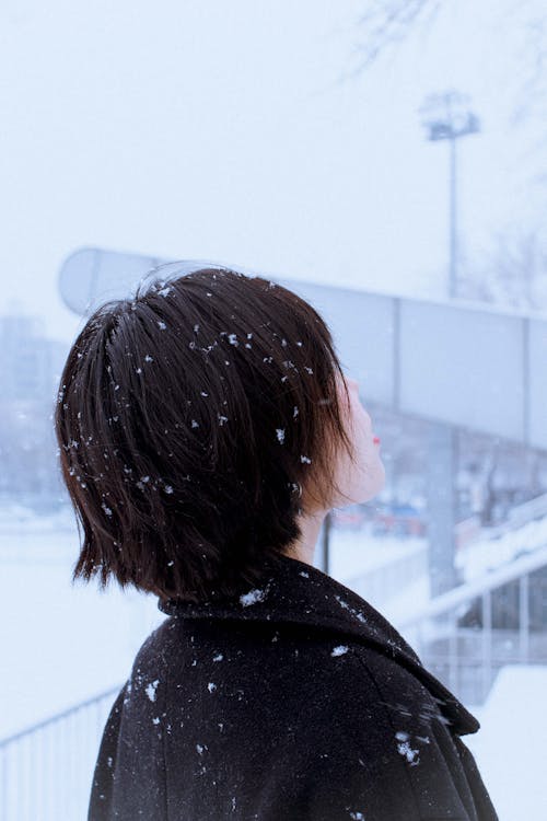 女人站在雪地裡，抬起頭，穿著黑色長外套