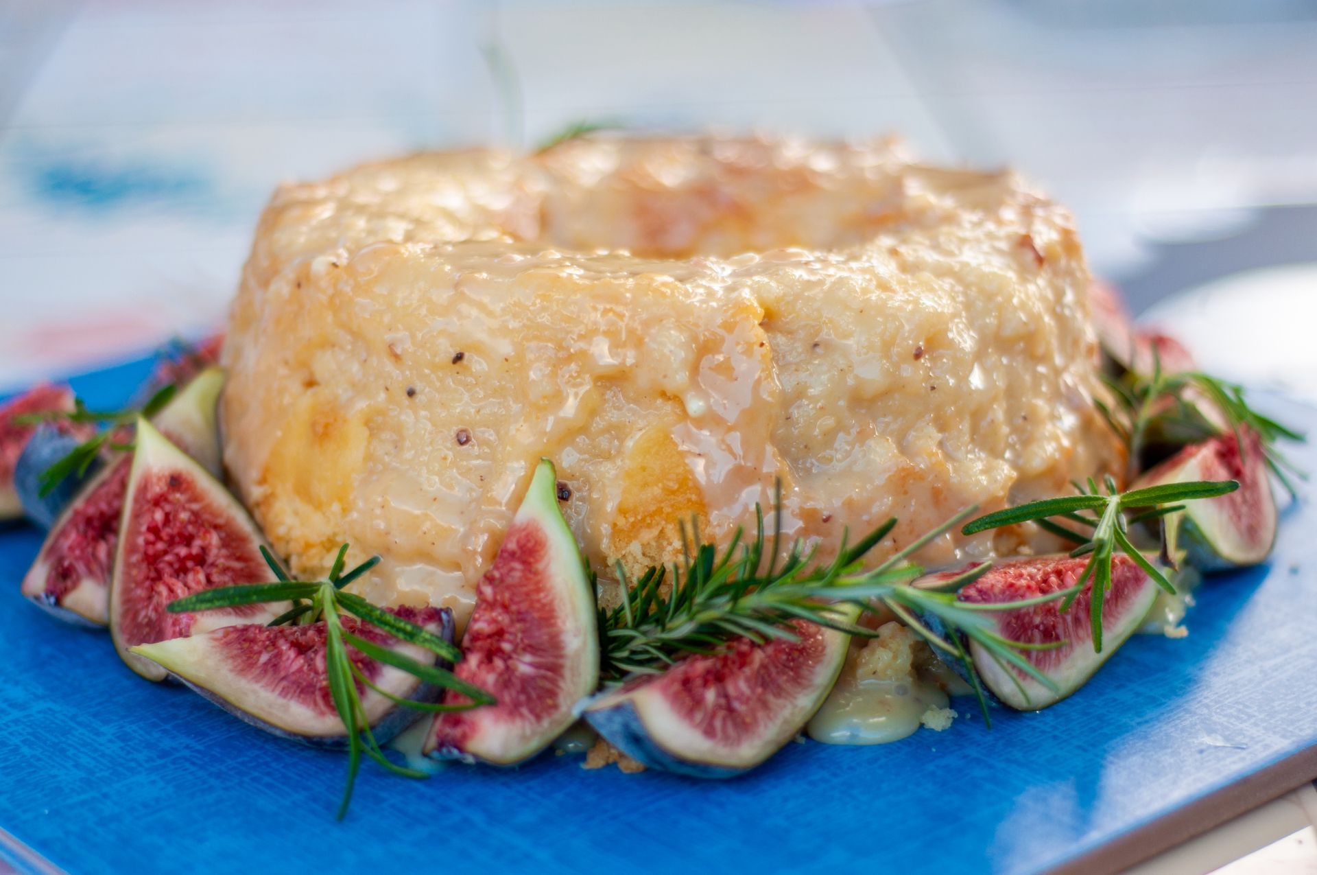 Close-up of a delectable cheese cake garnished with fresh figs and rosemary, presented on a blue board.