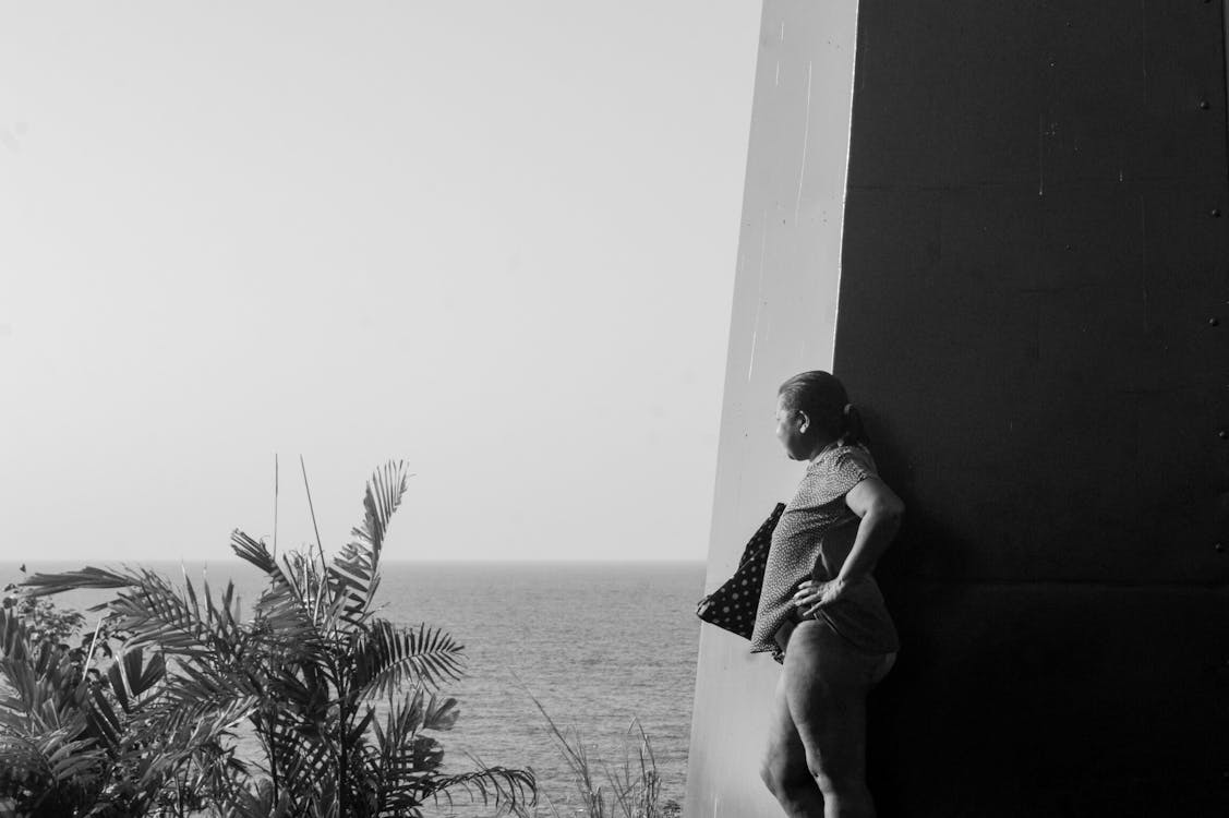 Black and White Photo of a Woman Leaning against a Wall and Looking at the Sea 