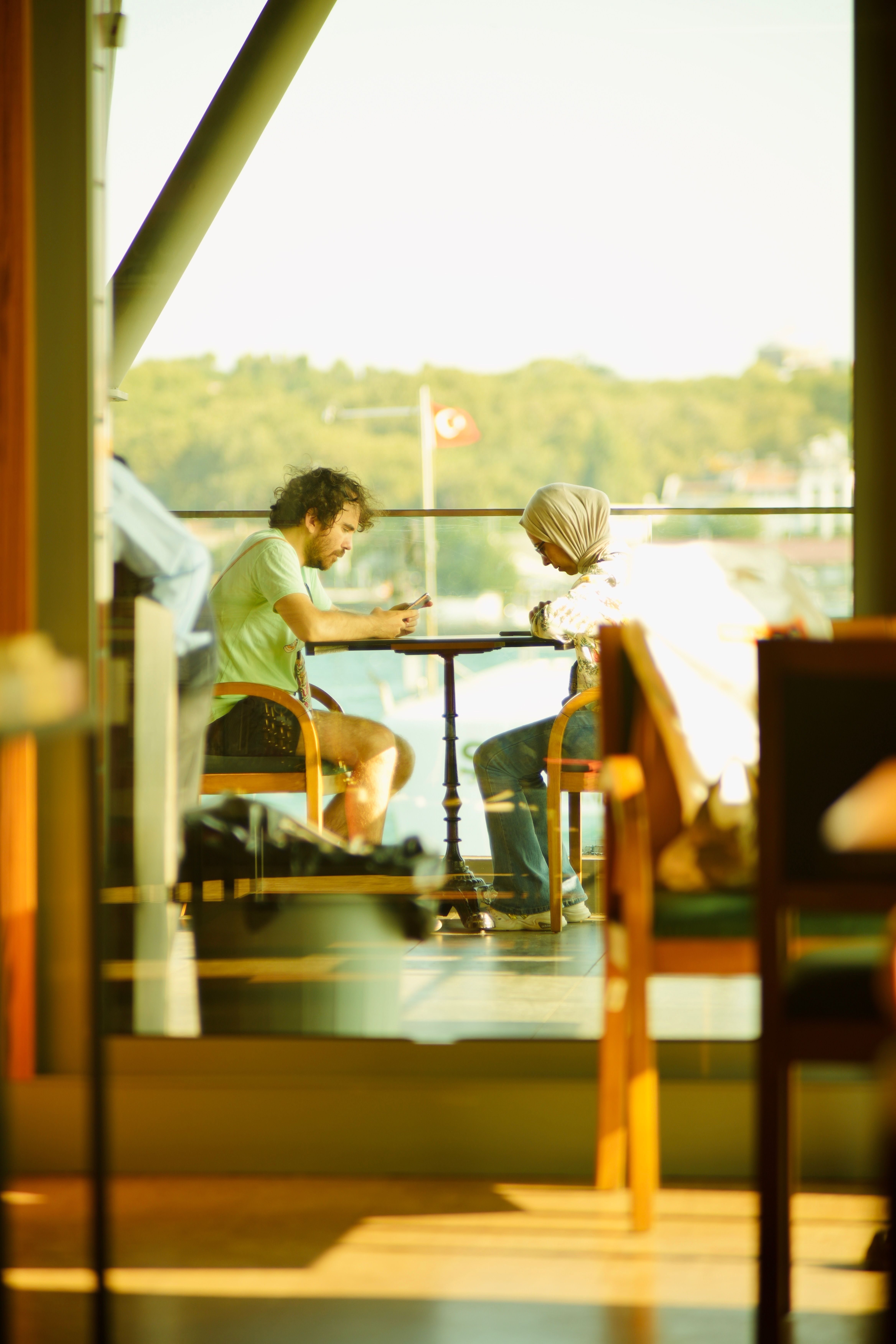 Two people engaged with smartphones at an outdoor café table, daylight setting.
