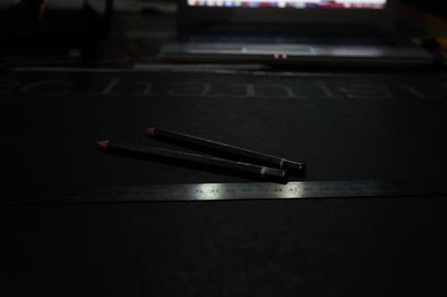 Черный карандаш рядом с серой стальной линейкой