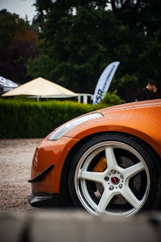 Orange sports car wheel with raindrops, captured close-up at an outdoor event.