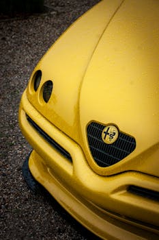 Detailed close-up of a yellow Alfa Romeo car wet with raindrops, showcasing automotive design.