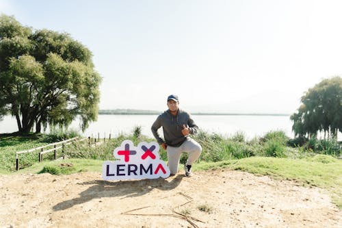 A Man Kneeling next to a Sign in Park by the Water 