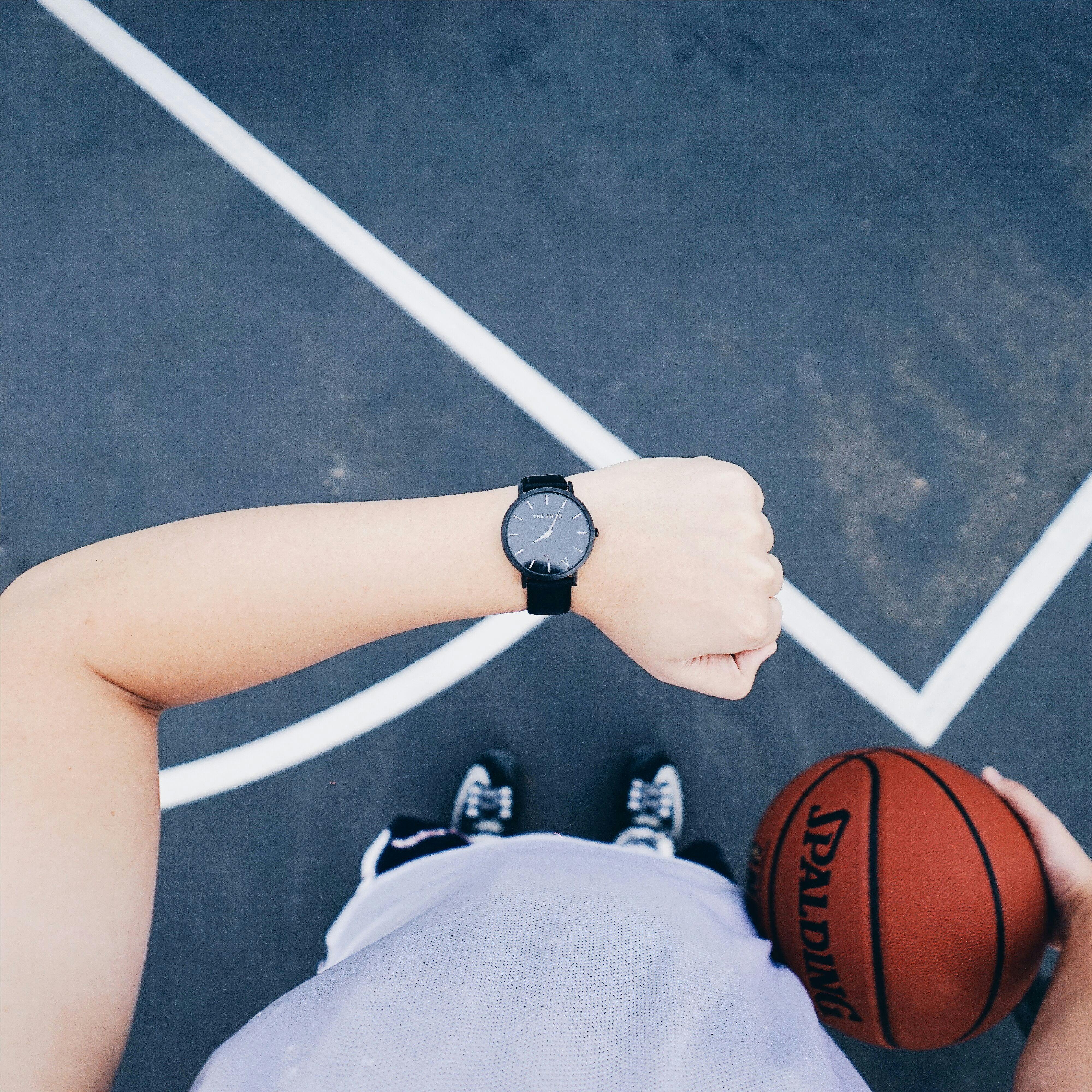 person wearing black round analog watch on left wrist while holding basketball on right hand