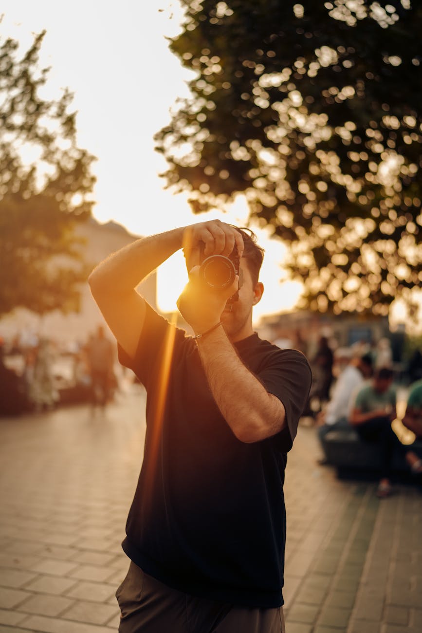 A photographer takes pictures at sunset with a golden lens flare in an urban setting.