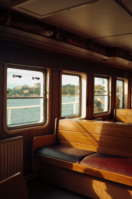 Warm sunlight streaming through windows highlights the wooden seats inside a ferry, creating a cozy atmosphere.