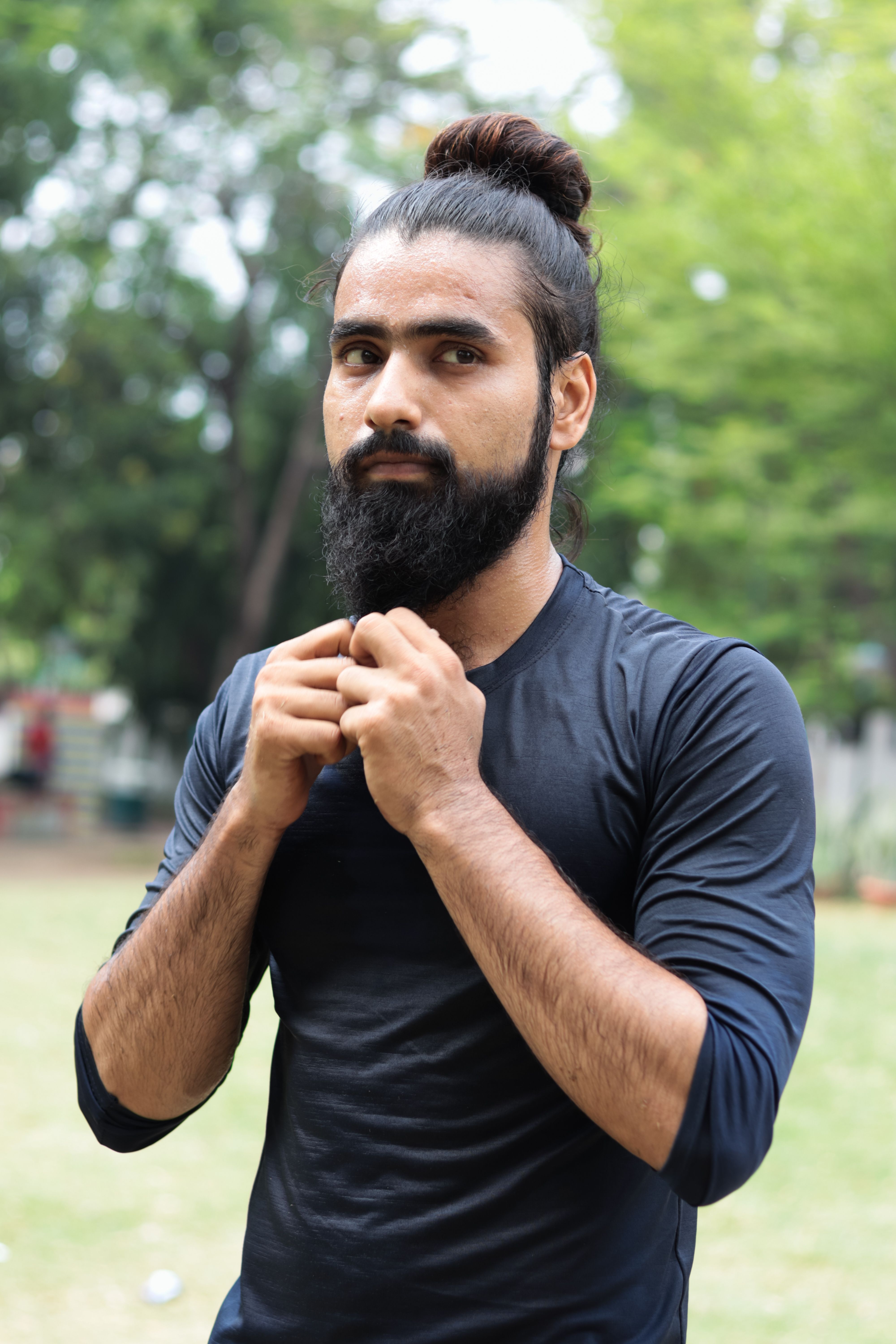 Portrait of a bearded man with updo outdoors in Patna, India. Casual attire with natural setting.