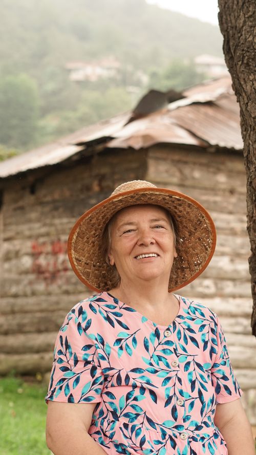 Free Charming portrait of a smiling elderly woman in a floral sundress and hat, enjoying a rural setting. Stock Photo