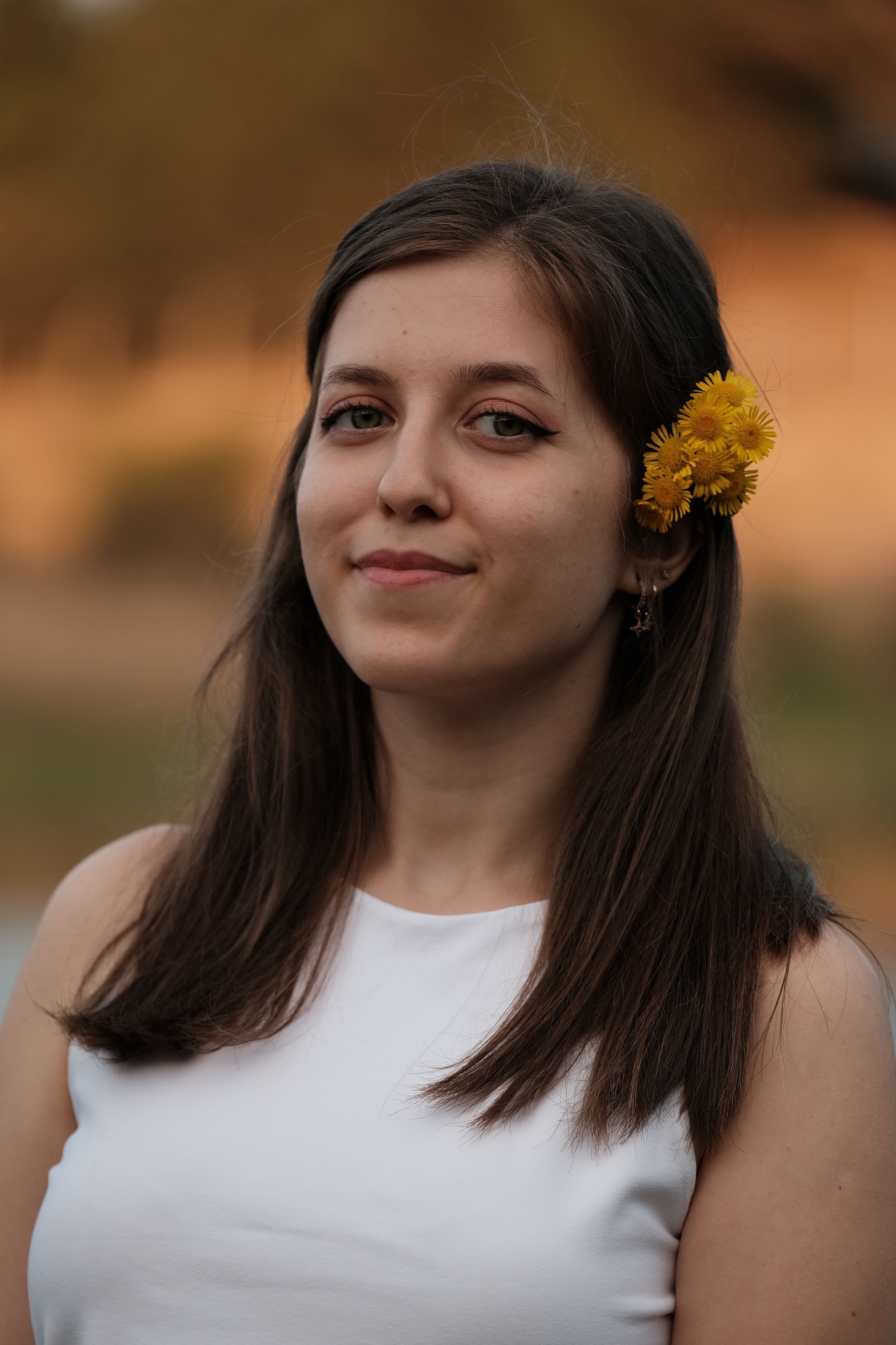 Close-up portrait of a smiling woman wearing white with a flower in her hair.