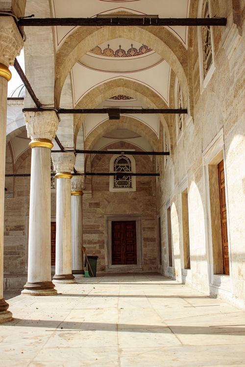 Free Sunlit mosque courtyard with classic colonnades and detailed arched ceilings, showcasing architectural beauty. Stock Photo