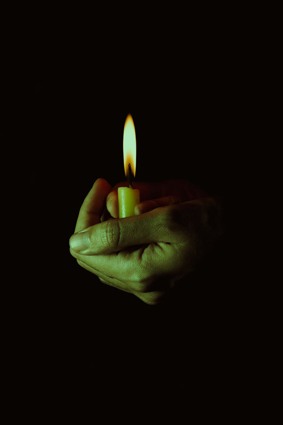 Close-up of hands cupping a lit candle flame, creating a warm glow in the dark.