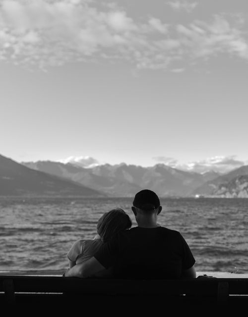 Free A couple sits peacefully on a bench by the lake, enjoying the scenic mountain view. Stock Photo