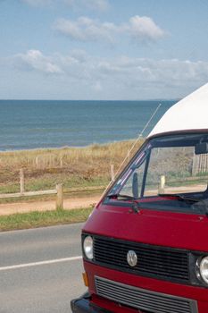 A vibrant red van parked on a coastal road with stunning sea views and clear skies.