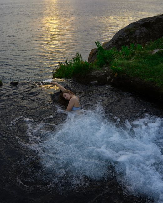 Young woman relaxes in a natural hot spring at sunset in Akureyri, Iceland.