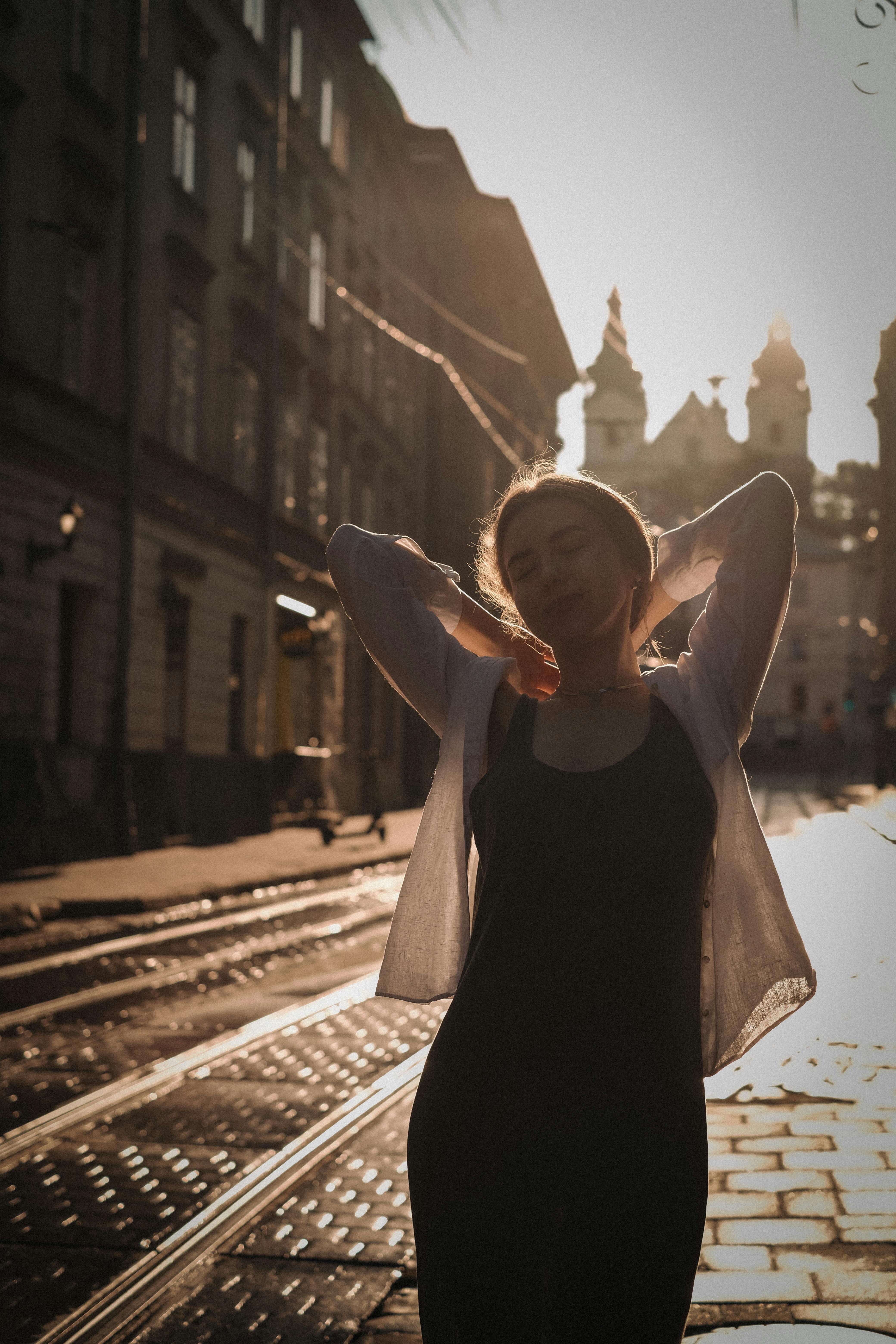 A young woman enjoys a sunlit walk on charming city streets, framed by classic architecture.