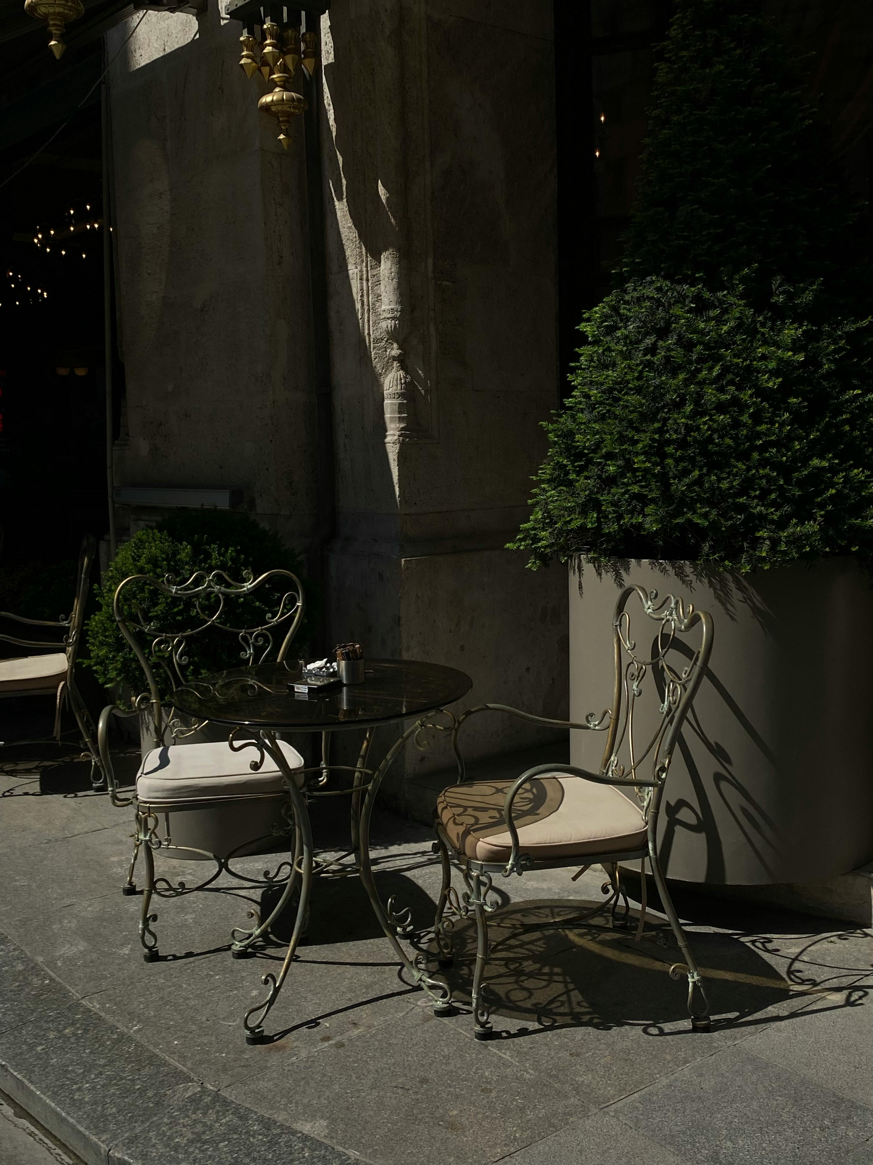 Charming outdoor café with ornate iron chairs on a city street corner.
