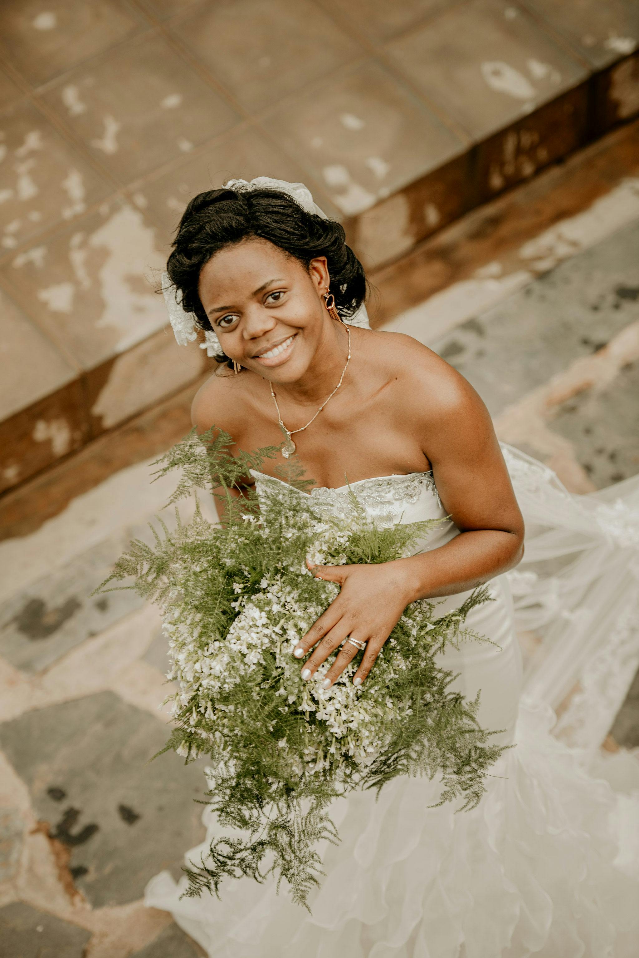 A smiling bride in a wedding dress poses with a bouquet, creating a joyful and elegant scene.