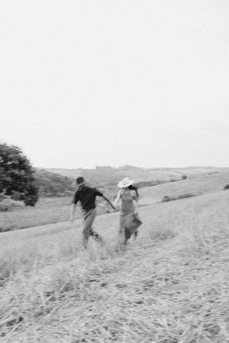 Woman And Man Holding Hands And Walking Together On Grassland