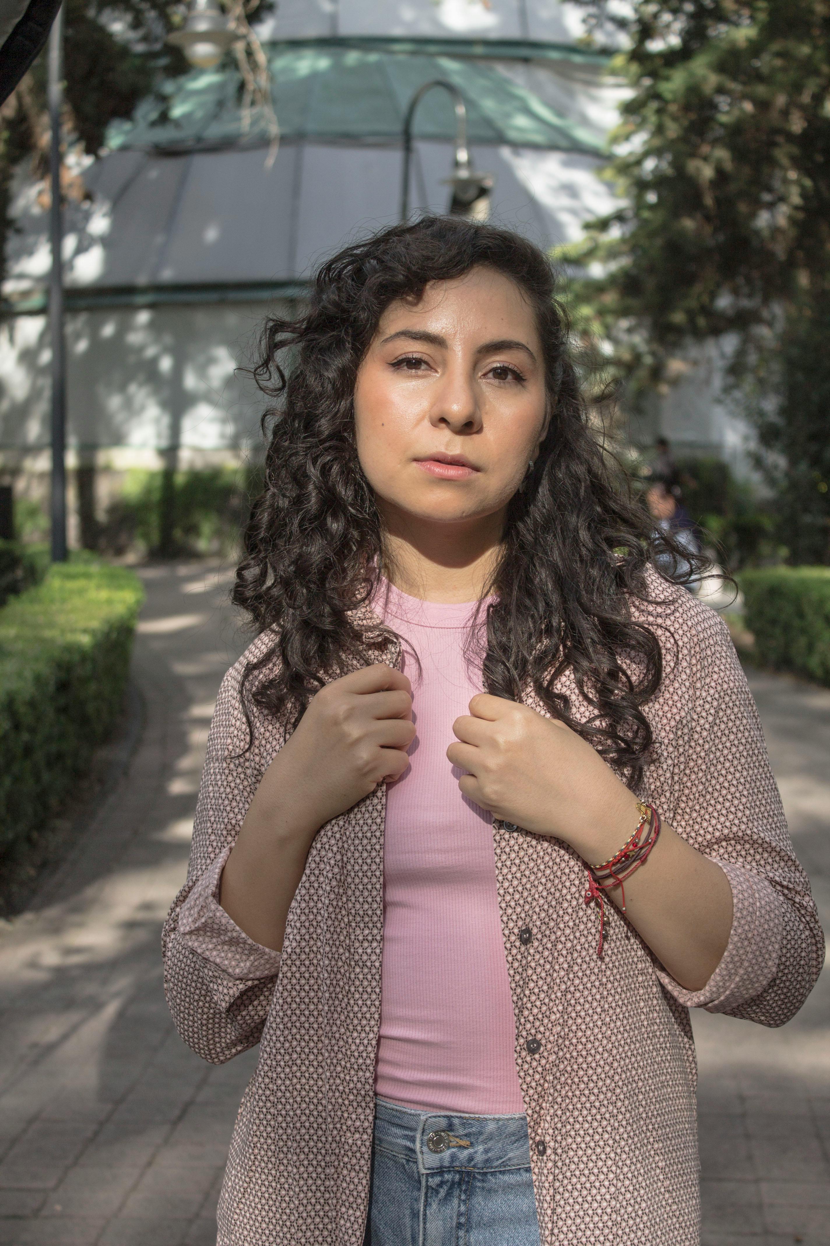 Portrait of a young woman standing outdoors in a sunlit park, exhibiting casual fashion.