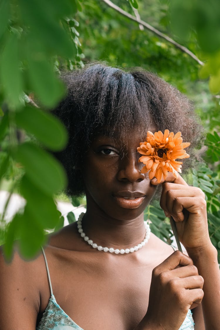 A Woman Covering Her Eye With An Orange Flower