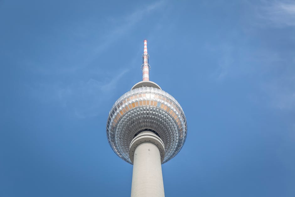 Low angle view of the iconic Berlin TV Tower under a bright blue sky.