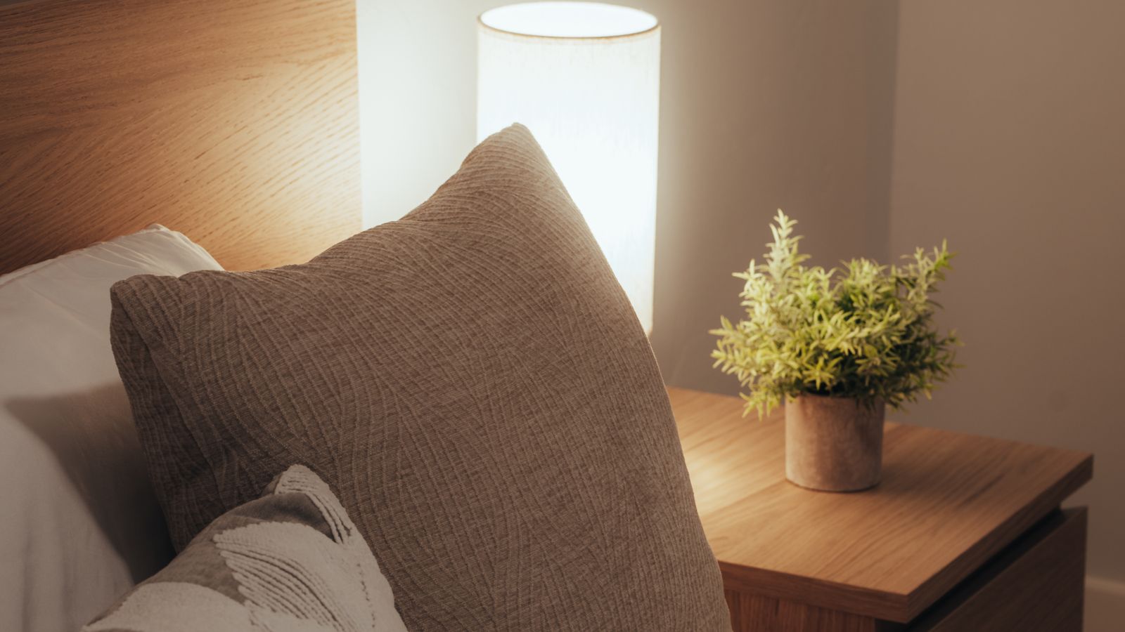 A warm bedroom with pillows, a bedside lamp and a wooden nightstand