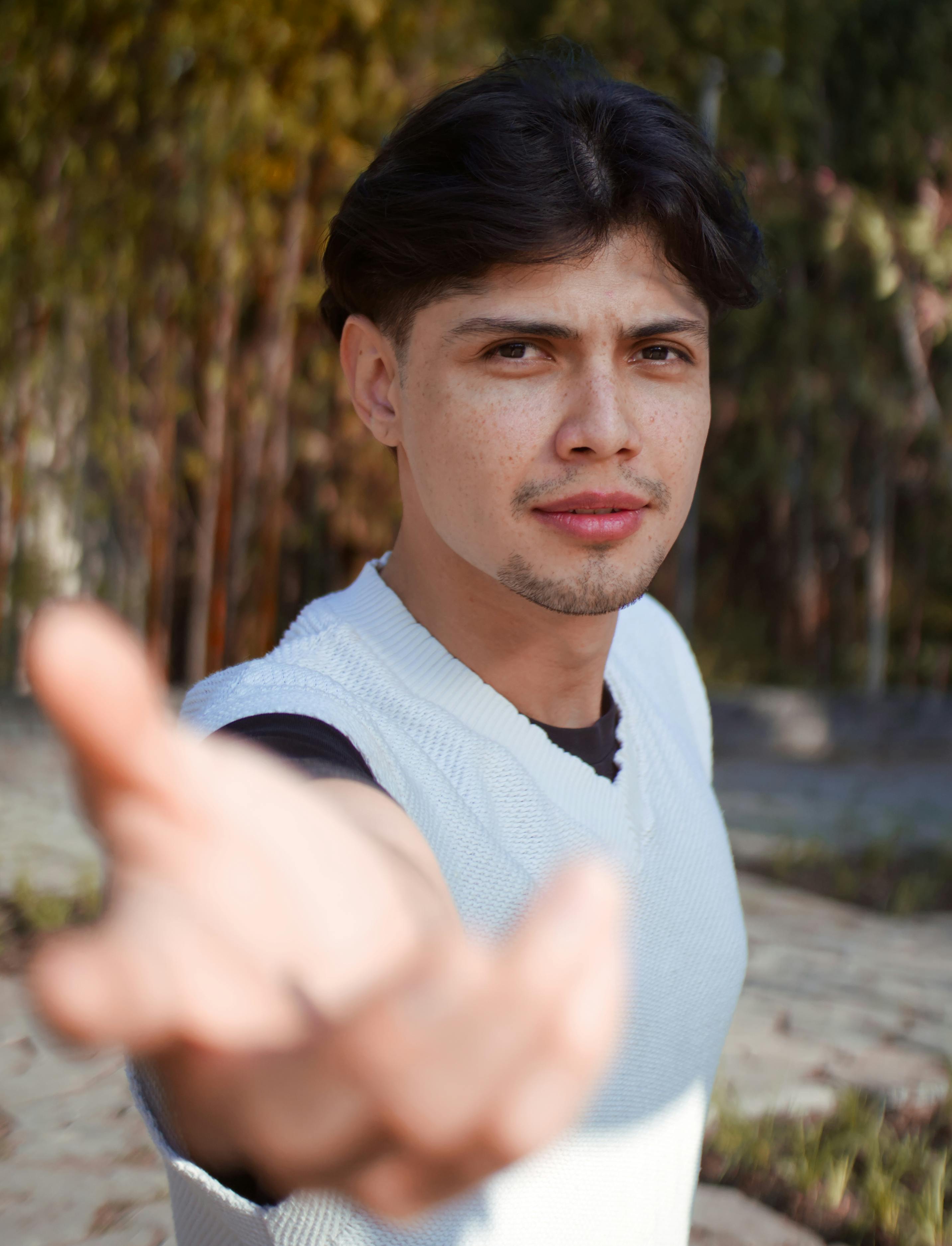 A young Hispanic man reaching out with a friendly gesture outdoors in a park.