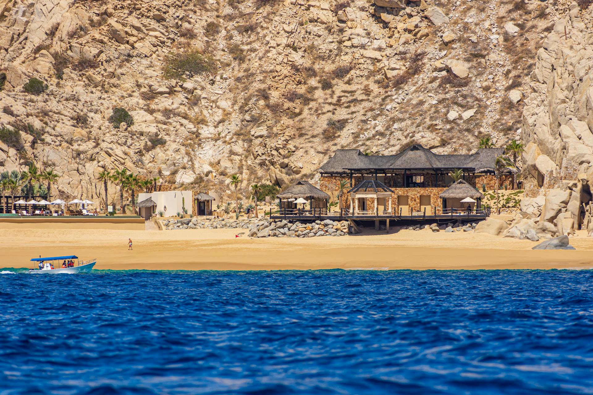 A luxury beachfront hotel nestled against rocky cliffs in Cabo San Lucas, Mexico.