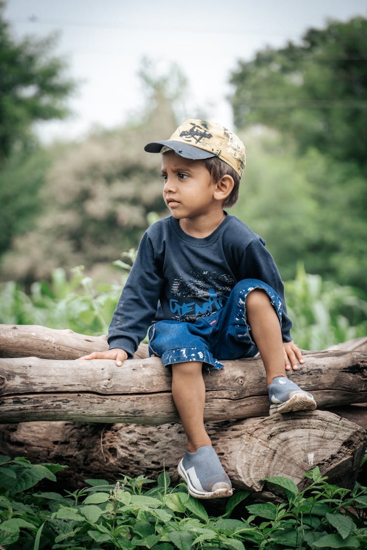 Boy Sitting On Tree Trunk In Forest