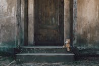 一只泰迪熊被遗弃在古老的乡村木门前，坐在台阶上